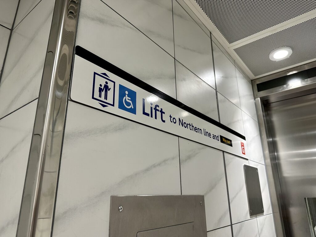 A station sign pointing to a step-free access lift, marked with the wheelchair symbol