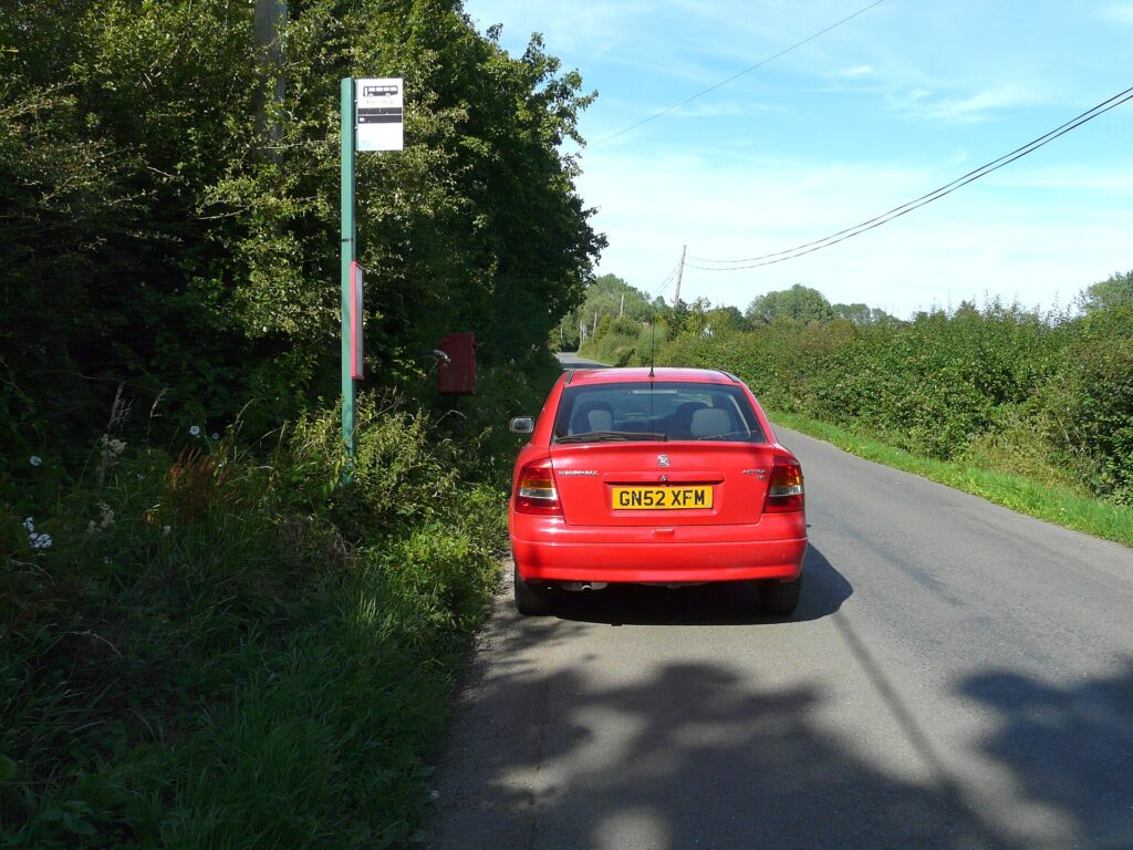 A car parked right beside a bus stop sign on a residential street