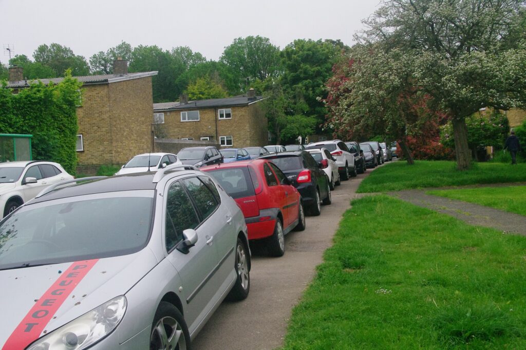 A line of cars parked on the pavement along a residential road in Harlow