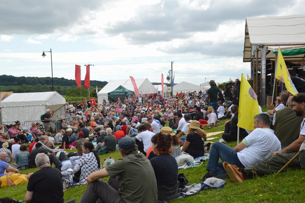 A large crowd sitting and standing on grass in front of an outdoor festival stage
