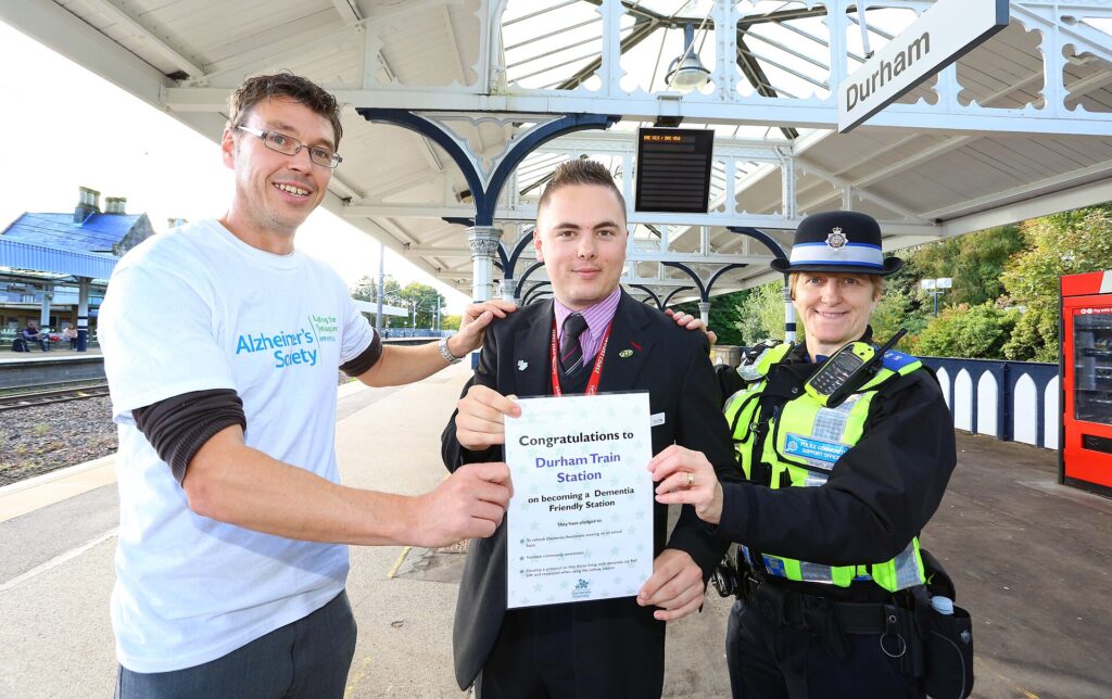 An Alzheimer's Society volunteer, a railway worker and a transport police officer hold a certificate on a station platform in Durham