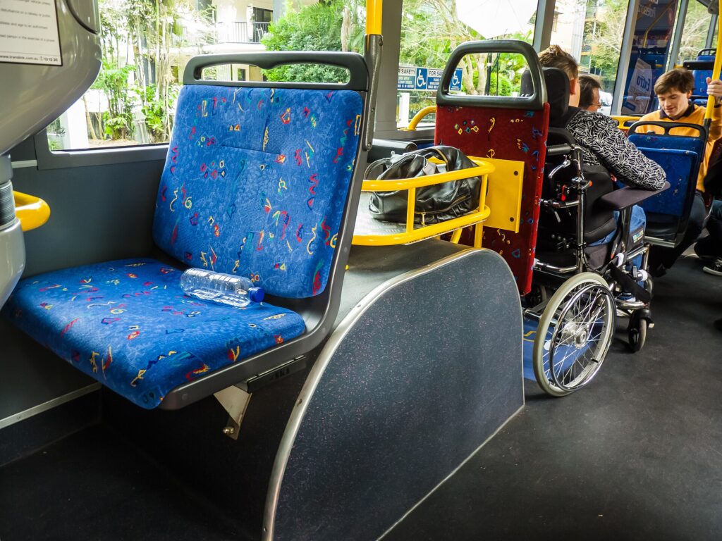 A wheelchair parked in the designated wheelchair bay of a bus beside the fold-down seats