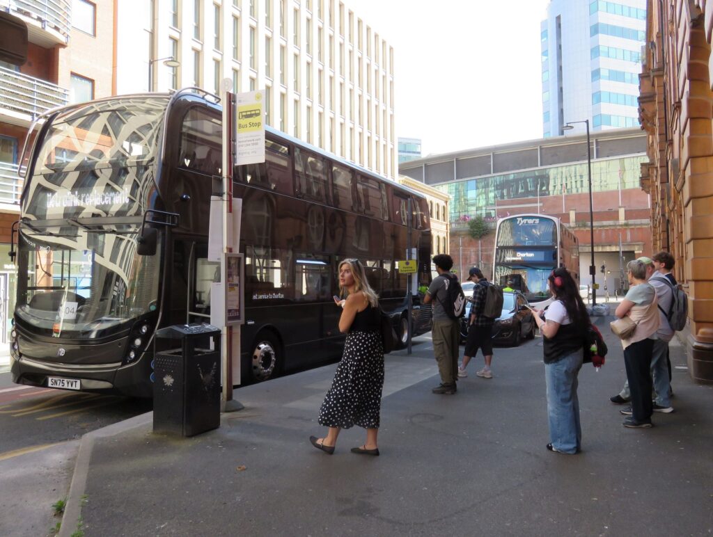 Passengers boarding replacement buses lined up at a stop in Manchester