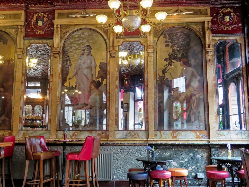An ornate Victorian pub interior with a long bar and a row of tall bar stools