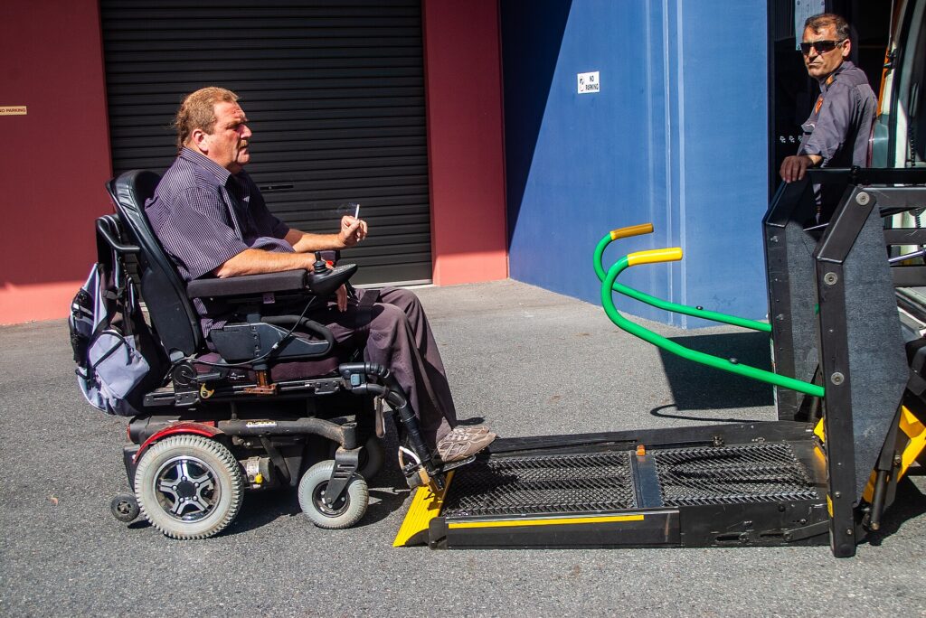 A man in a powered wheelchair on the hydraulic lift platform of an accessible taxi