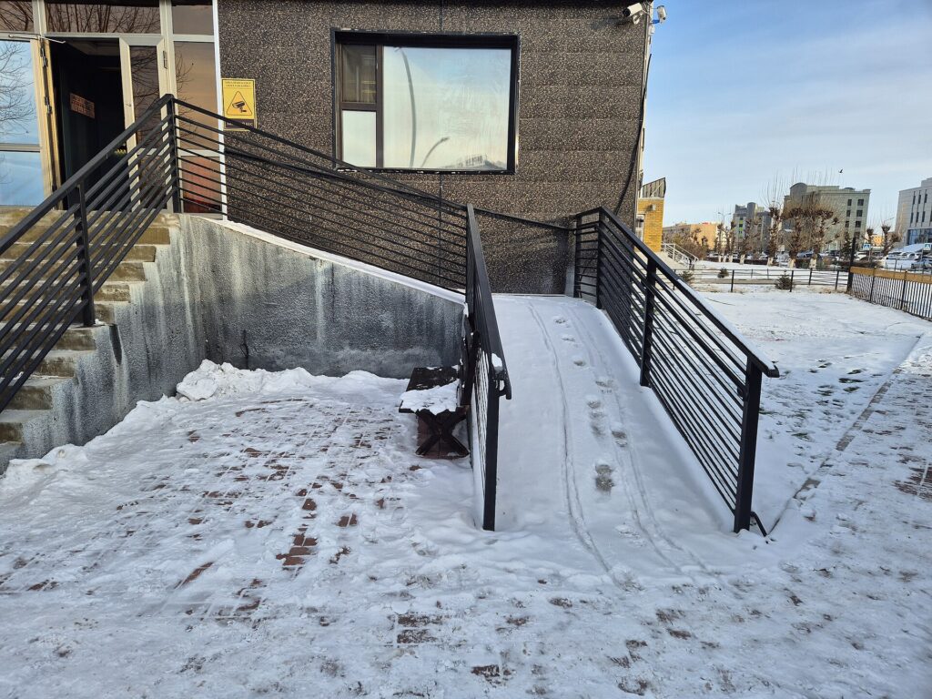 A wheelchair ramp with handrails completely covered in snow and ice